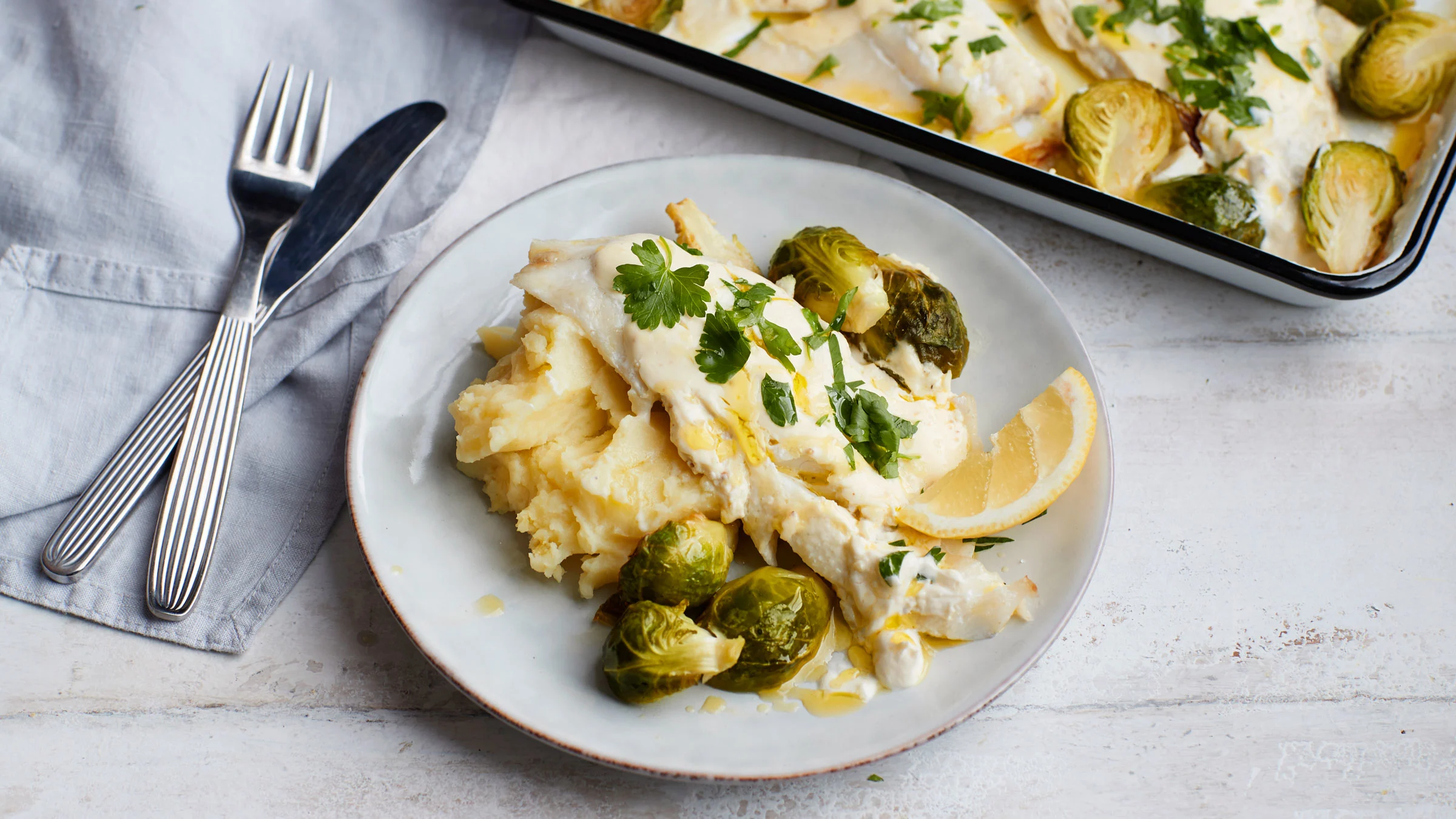 Smetanakuorrutteinen kuhafilee lautasella perunamuusin, ruusukaalien ja sitruunan kera