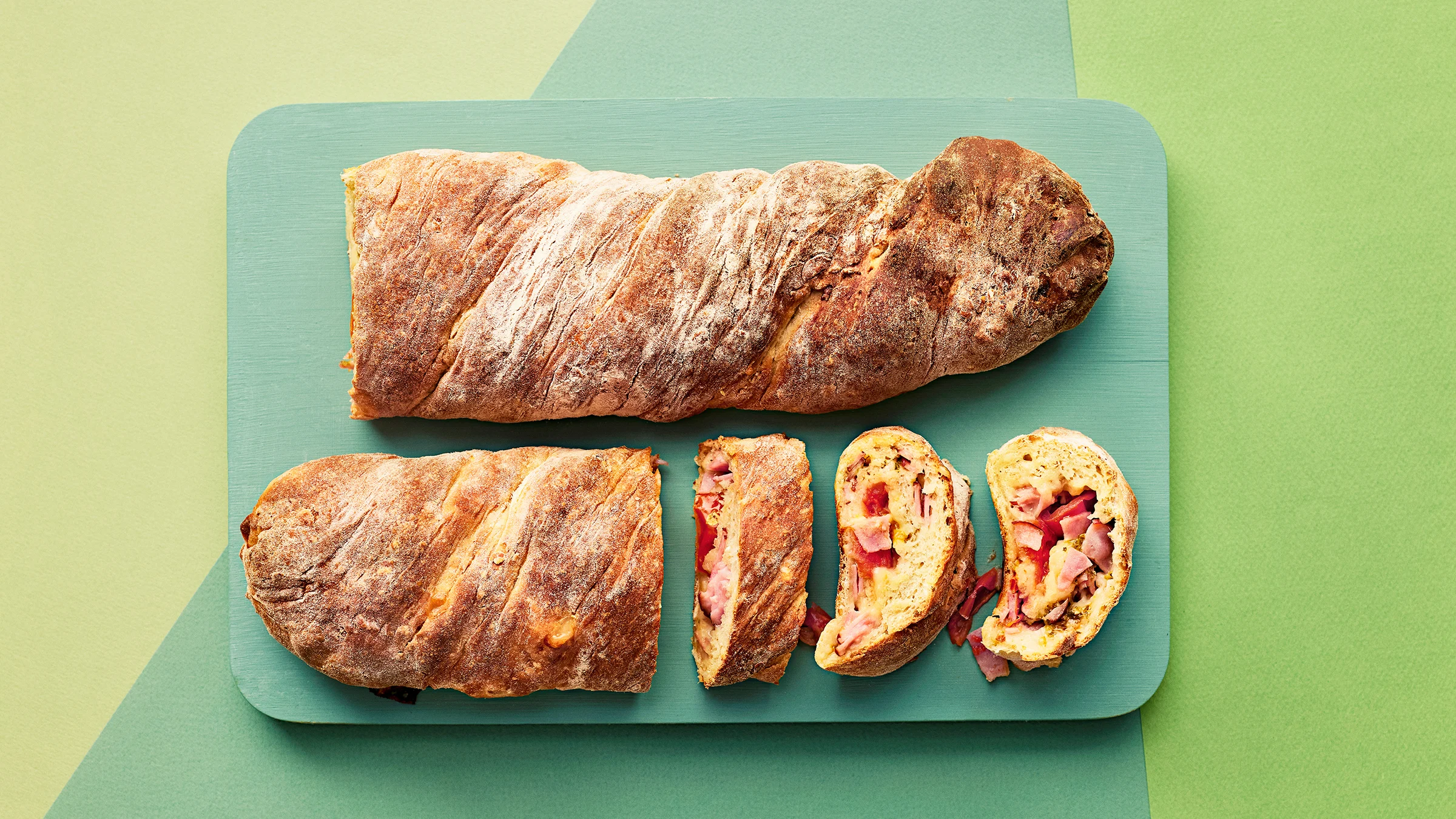 Täytetyt kaurapatongit vihreän leikkuulaudan päällä. Toisesta patongista leikattu kolme palaa.