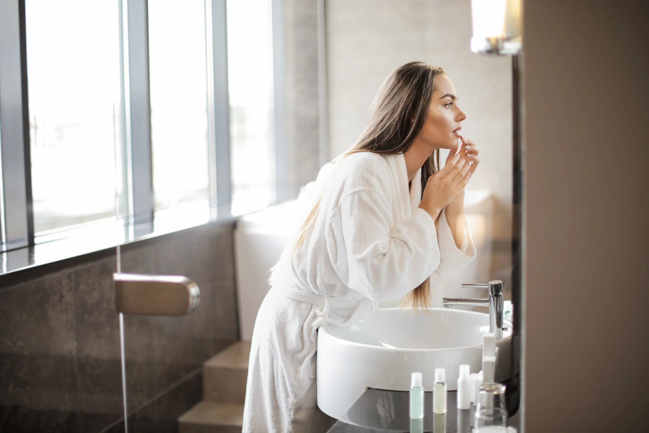 Kylpytakkiin pukeutunut nainen katsoo itseään peilistä