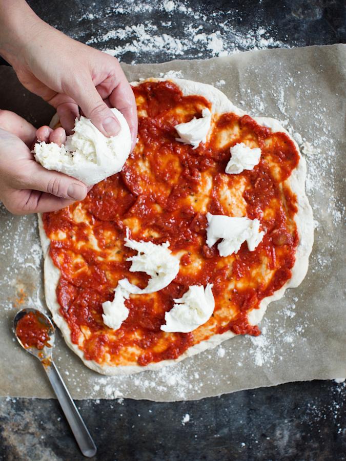 4\. Levitä tomaattikastike pohjalle. Revi peh-meää mozzarellaa sinne tänne tomaattikastikkeen päälle. Älä peitä koko pizzaa juustolla! Lisää muutama kirsikkatomaatti. Pakasta ylijäänyt kastike seuraavaa kertaa varten.