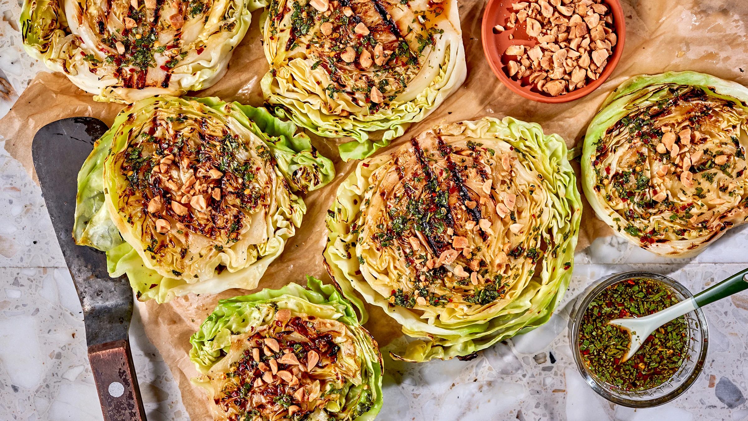 Grillattu varhaiskaali chili-sitruunakastikkeella. Vieressä paistinlasta sekä kastiketta ja suolapähkinöitä omissa kulhoissaan.