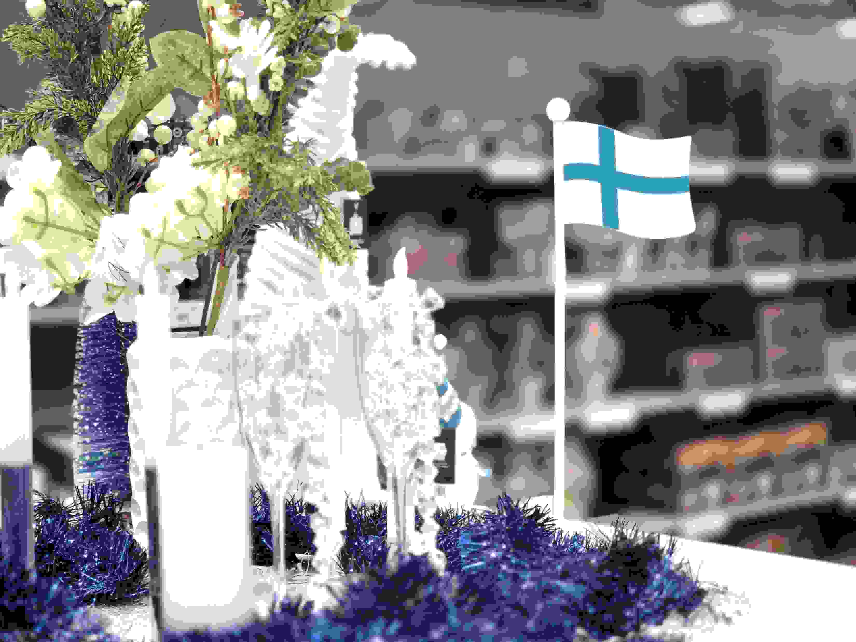 Itsenäisyyspäiväteemaisia tuotteita Prismassa. Pöydällä muun muassa kynttilöitä, kukkia ja puinen Suomen lippu.