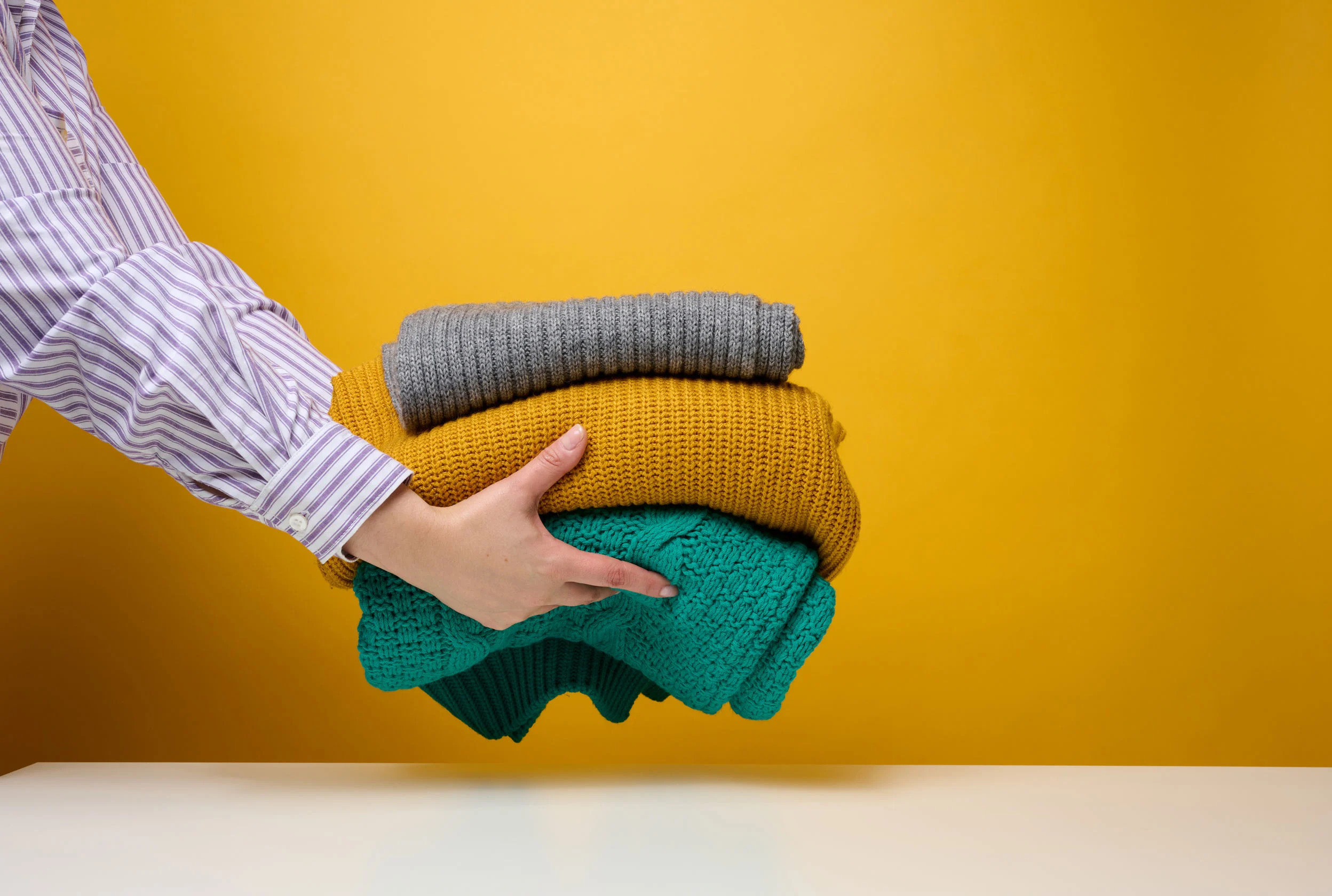 Nainen pitelee käsissään kolmea villapaitaa.