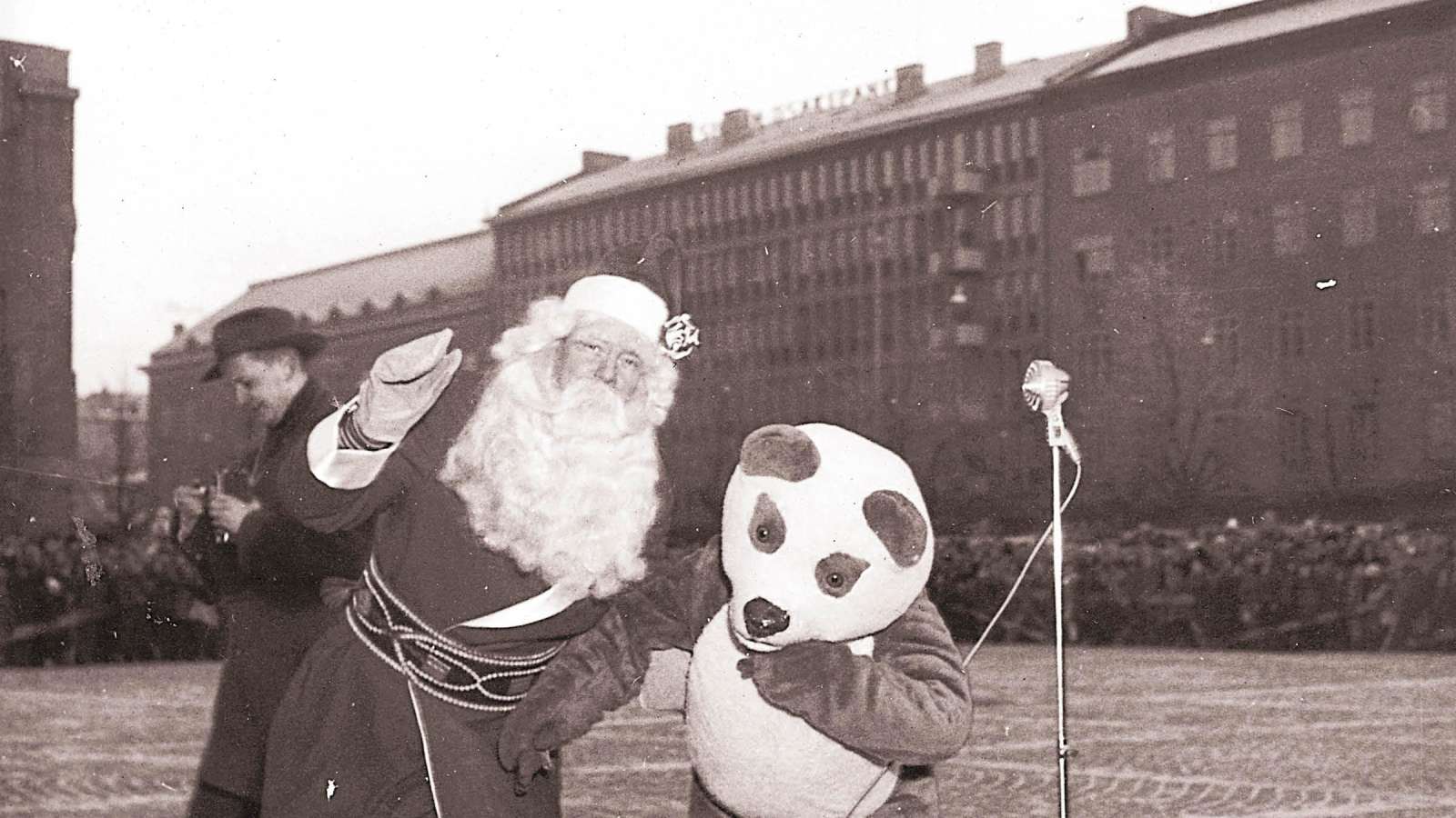 Joulupukki ja pandapukuinen hahmo seisovat torilla, taivaalla pörrää vanhanaikainen helikopteri