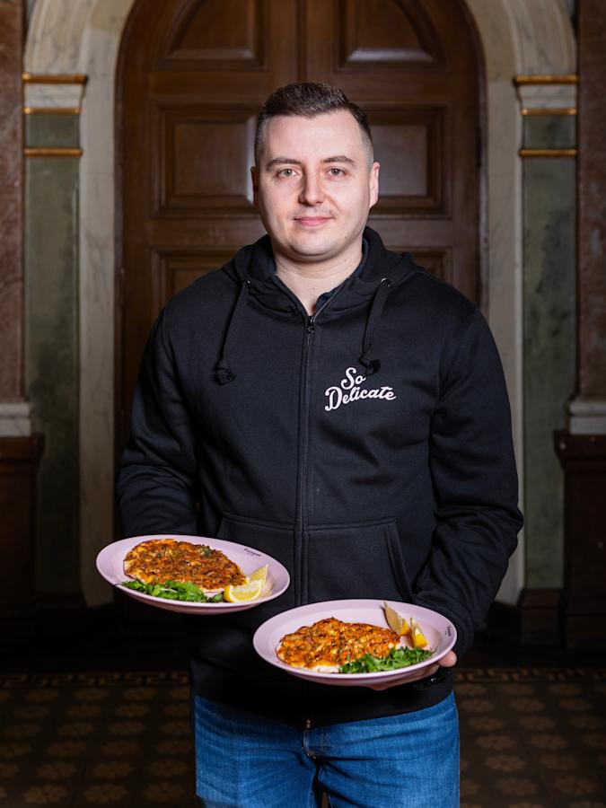 Spiros Halaris pitelee käsissään kahta lautasta, joilla on hiivatonta ohutleipää. Päällä musta paita ja jalassa siniset farkut.