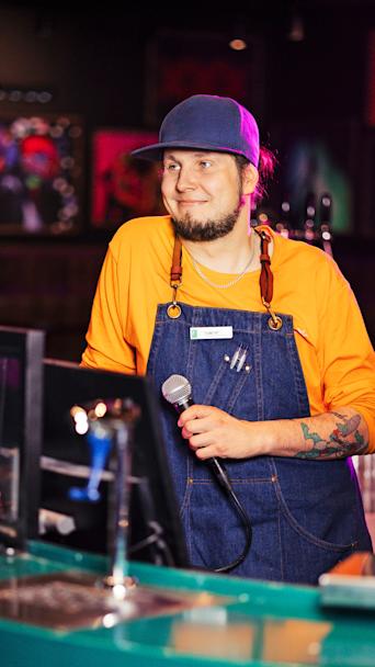 Karaokeisäntä Tomi Paakkunainen hymyilee mikrofoni kädessä.