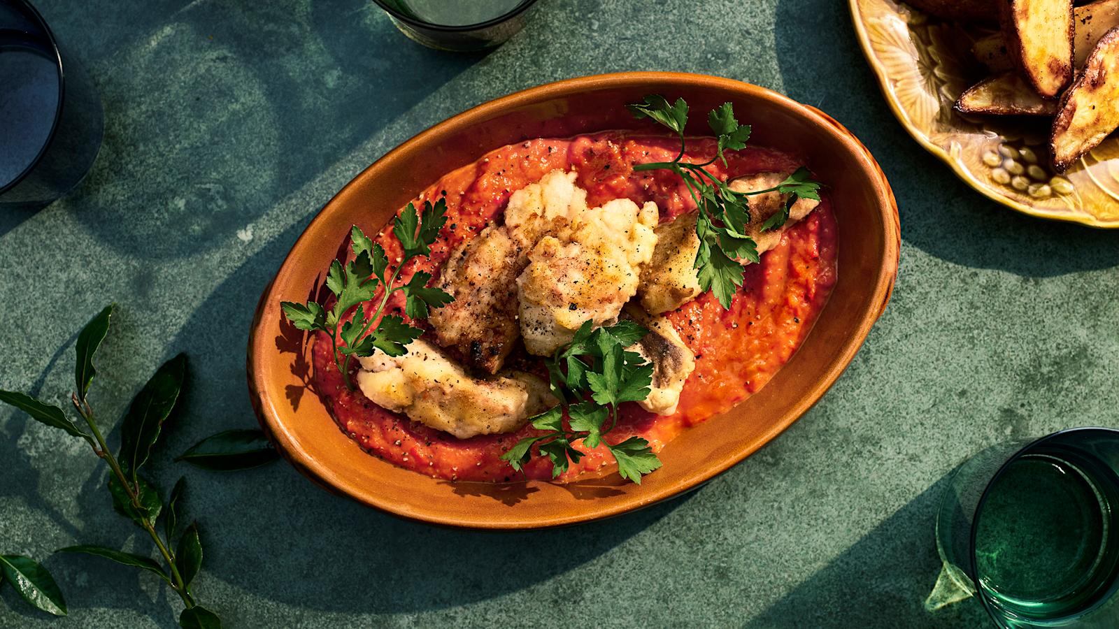 Paistettua seitiä ja paprikakastiketta oranssissa tarjoiluastiassa. Päällä lehtipersiljan oksia.