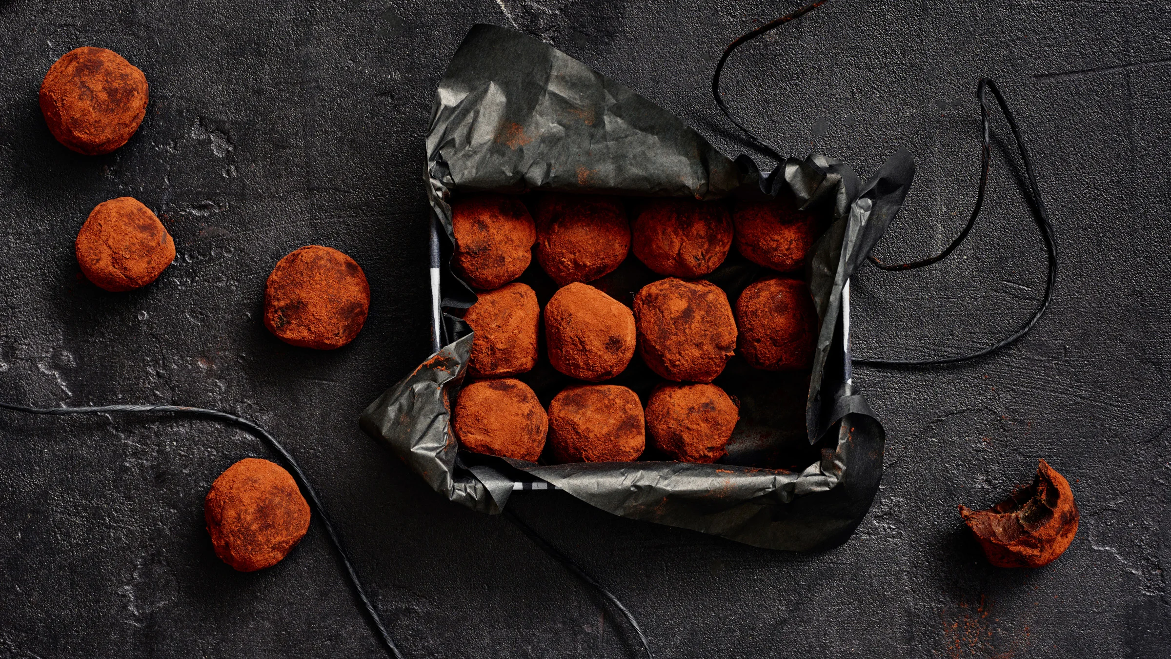 Pyöreitä kaakaojauheella päällystettyjä lakutryffeleitä tummassa lahjarasiassa ja pöydällä.