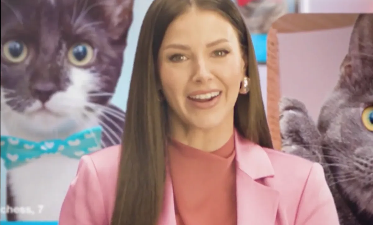 A still of Ariana Madix in a pink suit with pictures of cats in the background