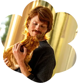 A man snuggling an orange cat in his arms