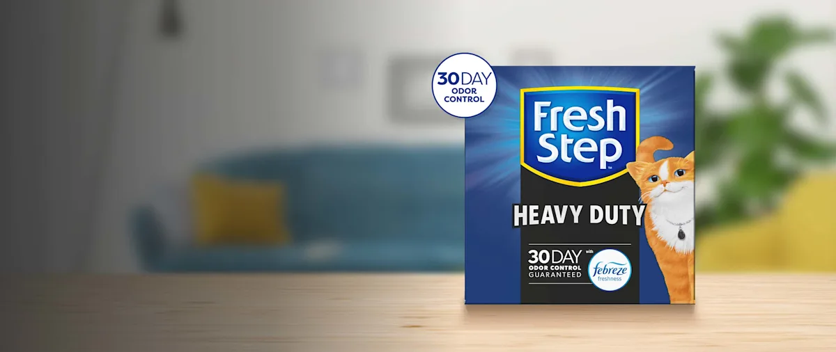 A box of Fresh Step Heavy Duty Cat Litter on a wood table with a blurred living room background
