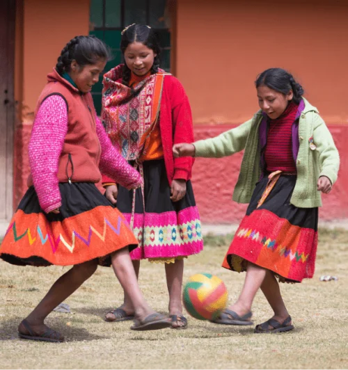 Three girls in traditional dress from Peru play soccer. 