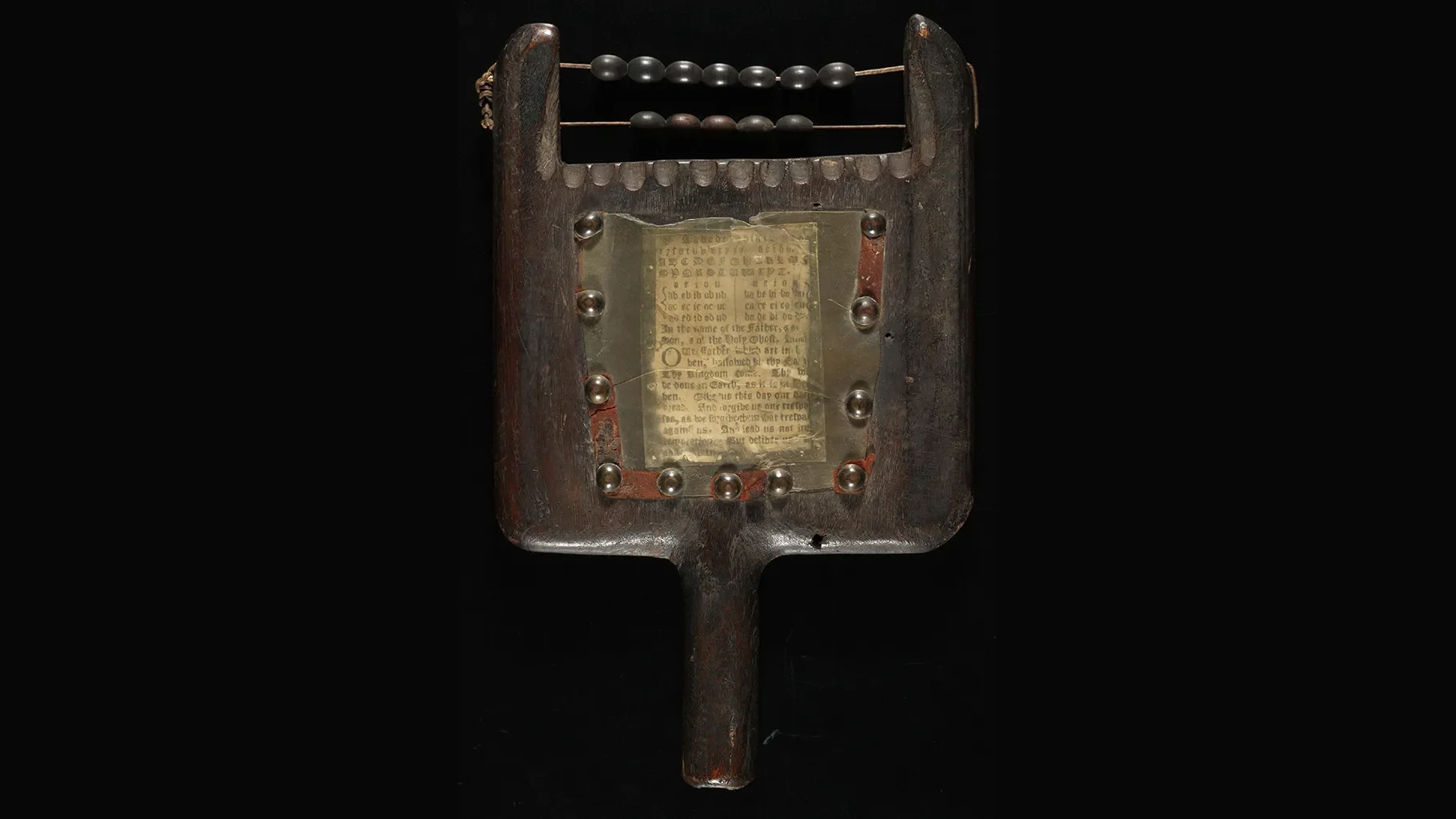A hornbook wasn’t a book at all, but a wooden paddle holding a single sheet of paper. Made about 300 years ago, this one shows letters and words protected by a thin, transparent sheet of animal horn. At the top is a small abacus for counting. Children learned words and numbers using the same object.