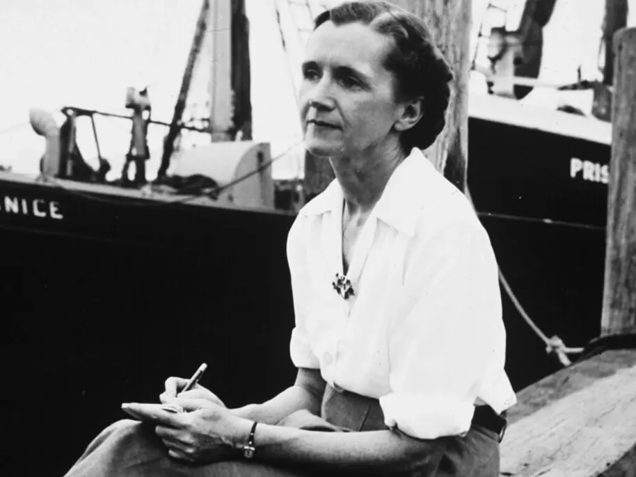 Rachel Carson, author of Silent Spring sitting in front of a boat and holding pen and paper