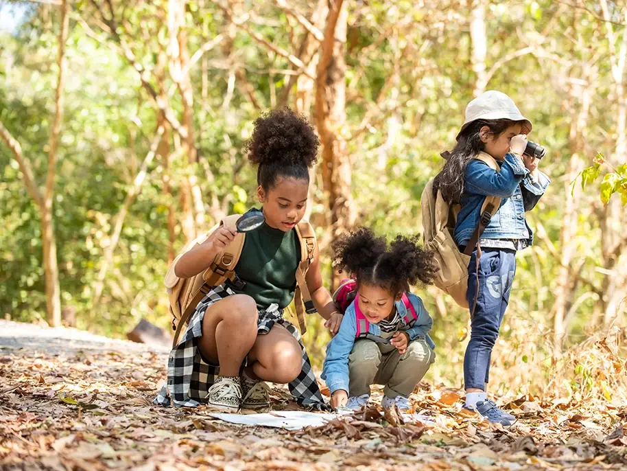 A group of children in the woods observe nature with binoculars, a magnifying glass and map.