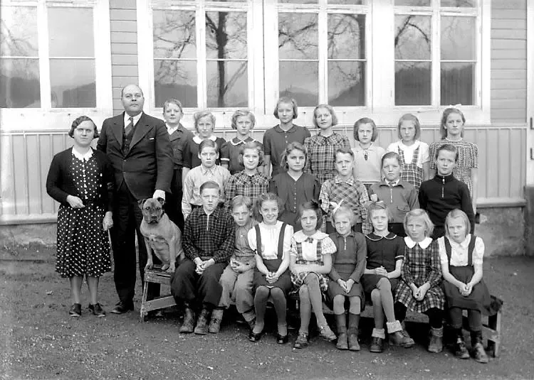 Sweden, 1940s: The Swedish Folkskola, or “people's school”, was founded in 1842 to give all kids a chance to learn, no matter who they were. Teachers like Karl Josefsson were very proud of their work. Here we see him standing with his wife and students in front of the schoolhouse where he also lived. Can you spot an unusual student in the picture?