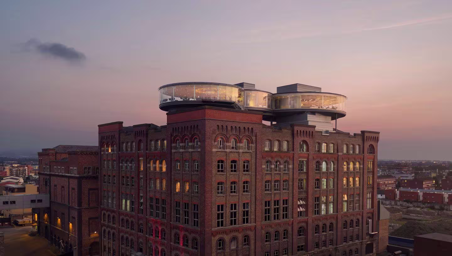 Historic brick mill building at dusk with two illuminated circular glass rooftop pods overlooking the city.
