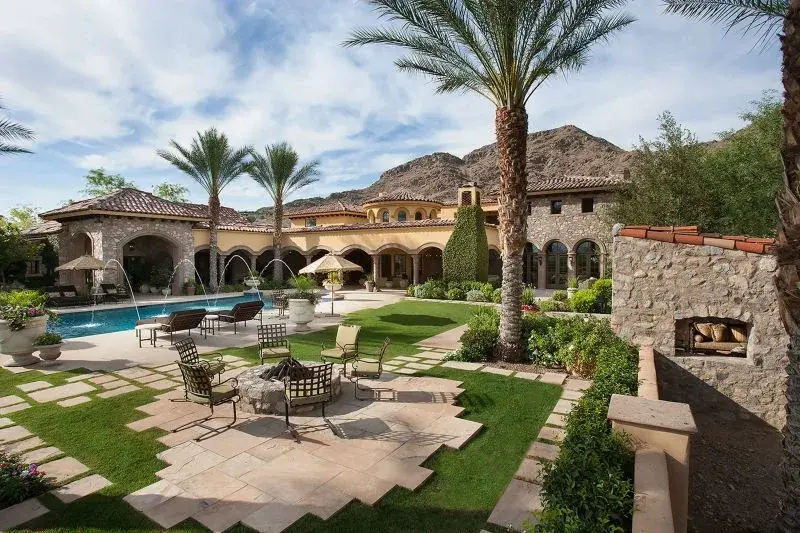 Lush palm trees, flowering plants, and a stone archway lead you to the intricate wood door and into 8055 North Mummy Mountain Road. Architecturally designed by Erik Peterson, this 5-acre Mediterranean estate features timeless details such as wrought iron 