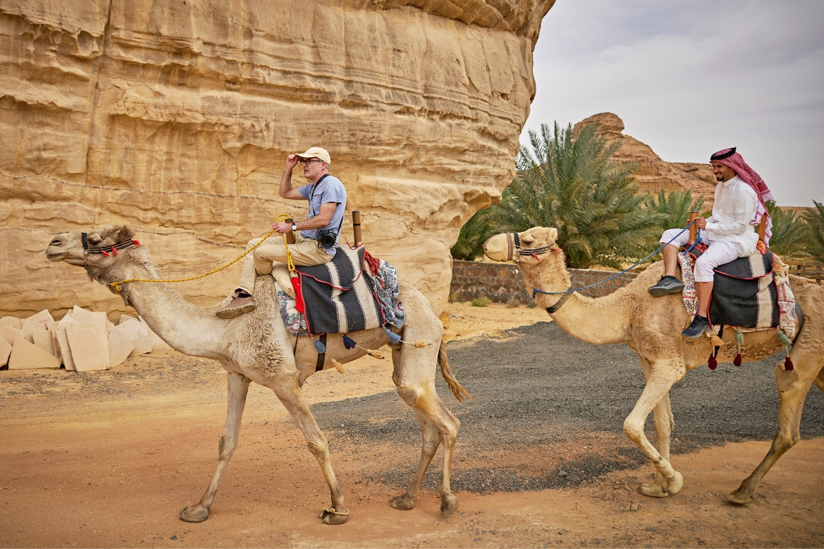 Bedouin man and tourist riding on camel, cultural travel while exploring Middle East desert