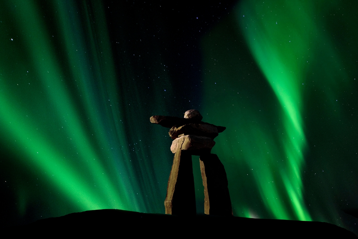Northern lights or aurora borealis with Inukshuk stone structure built by Inuit in the Arctic