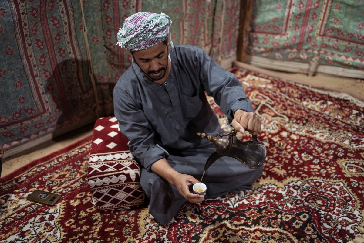 Bedouin man wearing traditional clothes preparing tea in a tent on a carpet in the Middle East desert