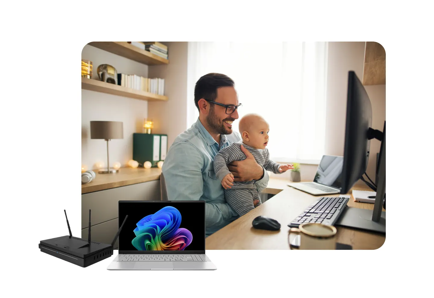 Man holding an infant in from of a computer monitor with a router and laptop in the foreground