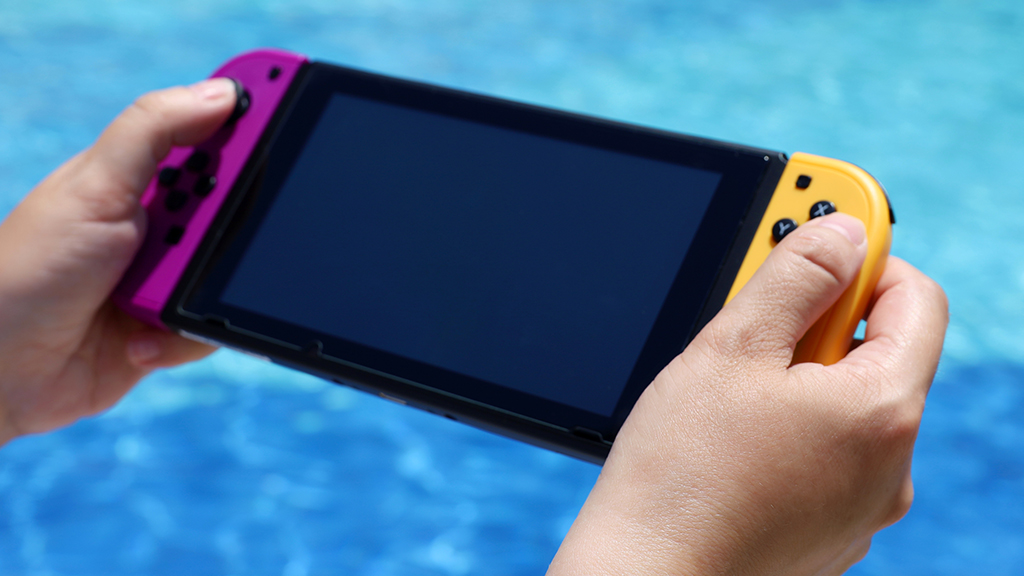 Person holding Nintendo Switch near pool