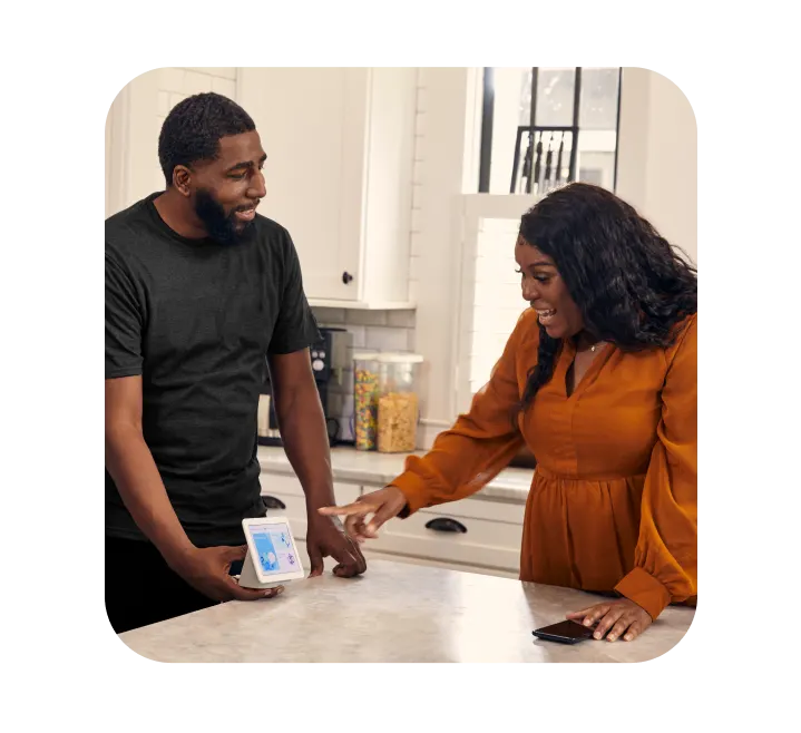 Man and woman looking at device in their home.