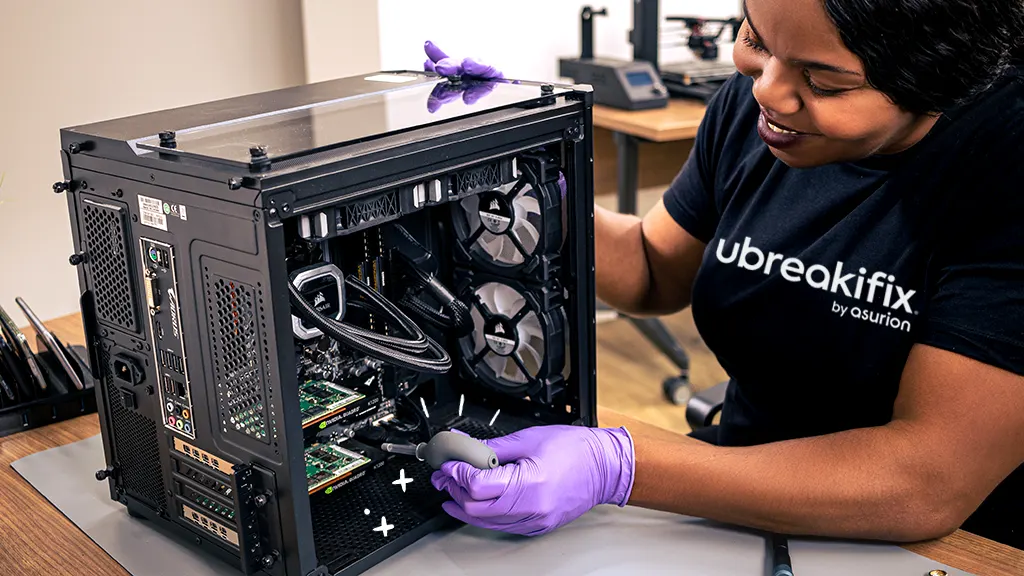Technician wearing purple gloves repairing a desktop computer tower at a workbench.