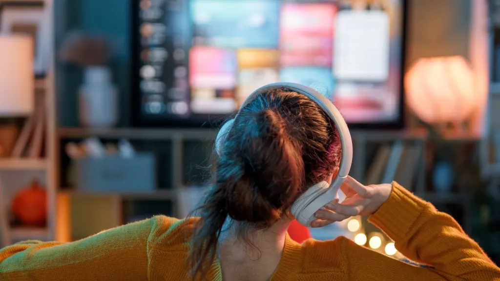 Back view of a young woman with headphones watching a TV with multiview