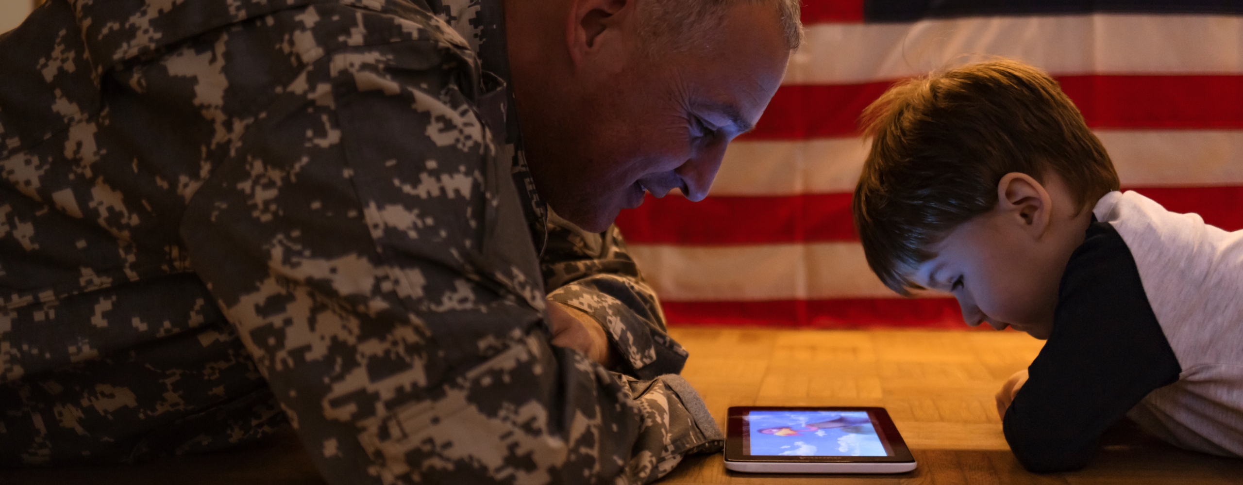 Dad in a military uniform looking at an ipad together with his son