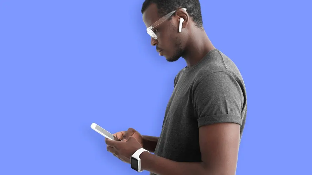 Man with glasses and wireless headphones looking down at smartphone