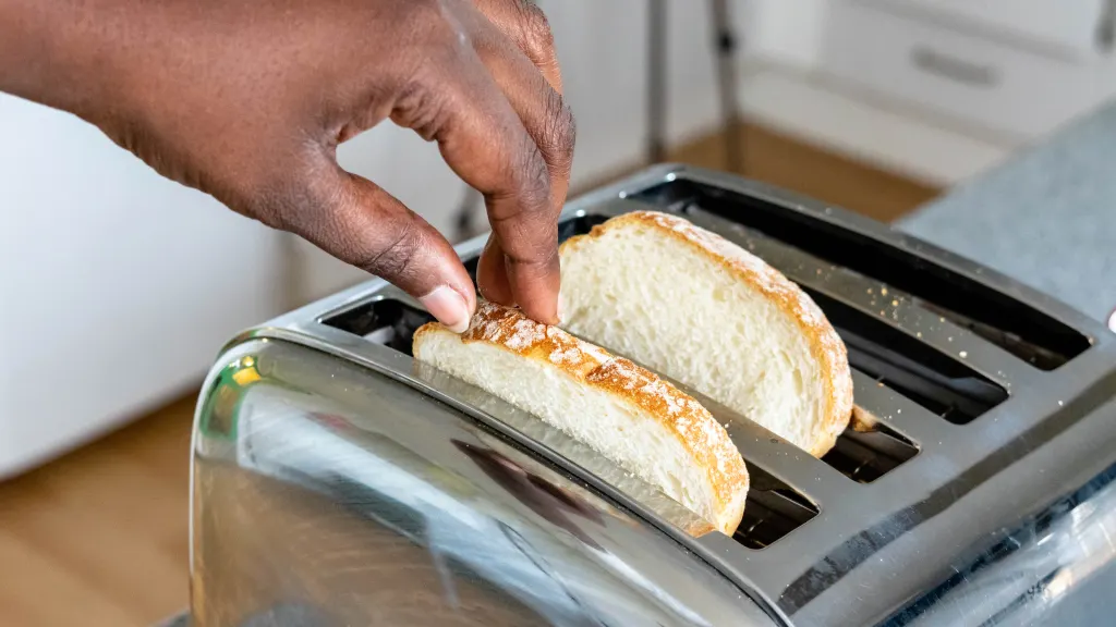 Close up of hands pulling toast out of a silver toaster