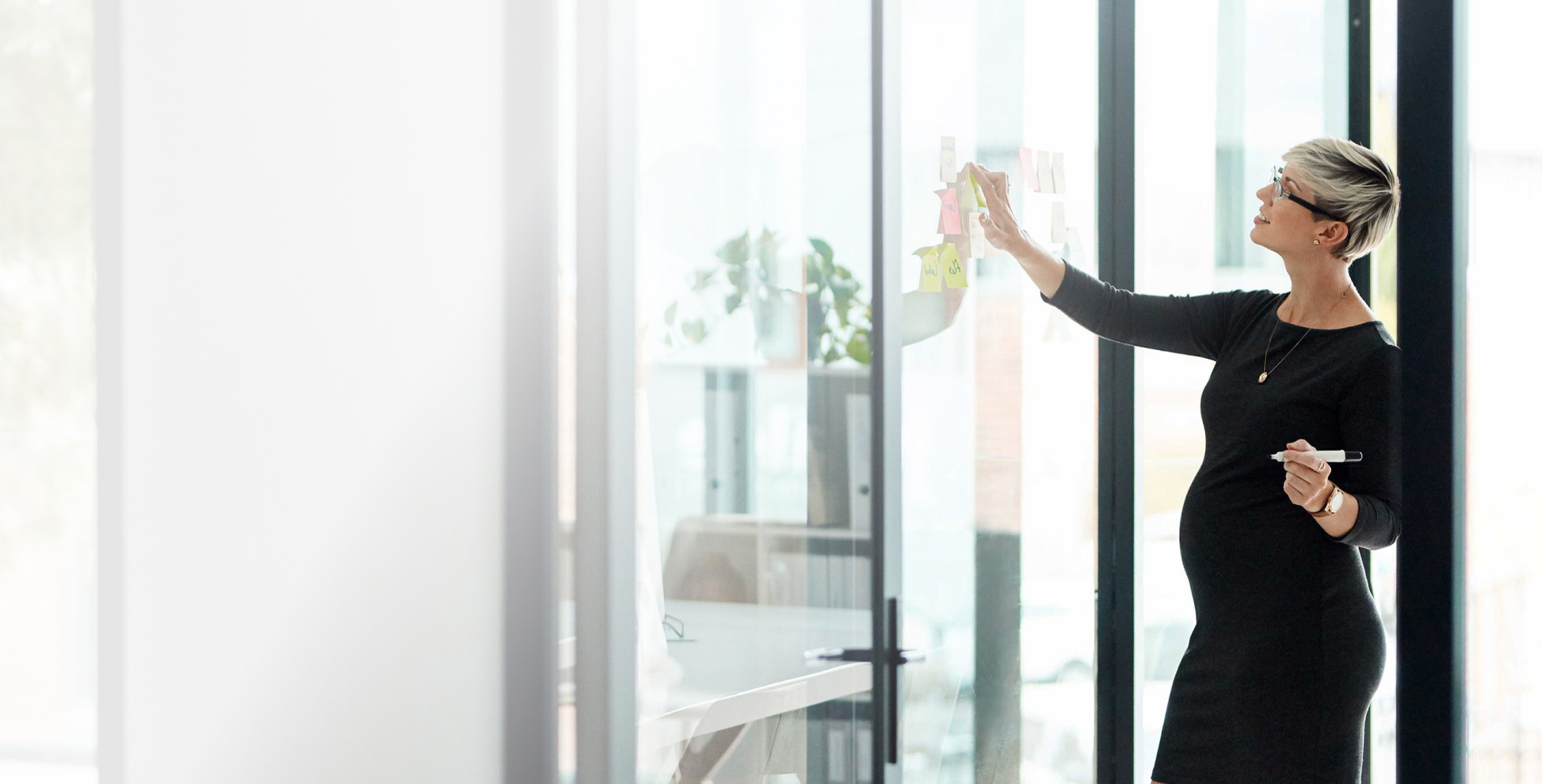 a pregnant businesswoman brainstorming with notes on a glass wall in an office
