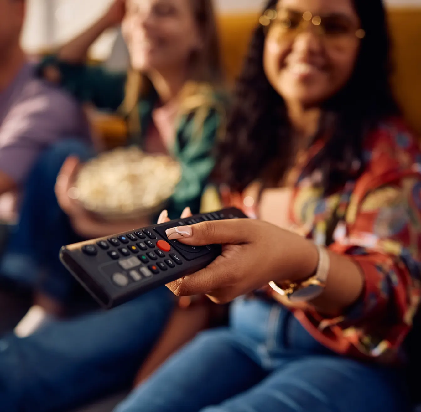 Person holding a TV remote while watching television with friends.