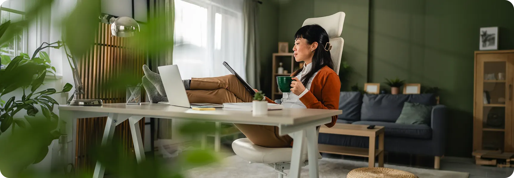 Woman relaxing at a home office desk using a laptop and tablet in a modern workspace