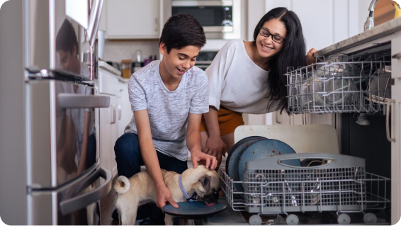 Mom and son use the dishwasher while the dog licks a plate