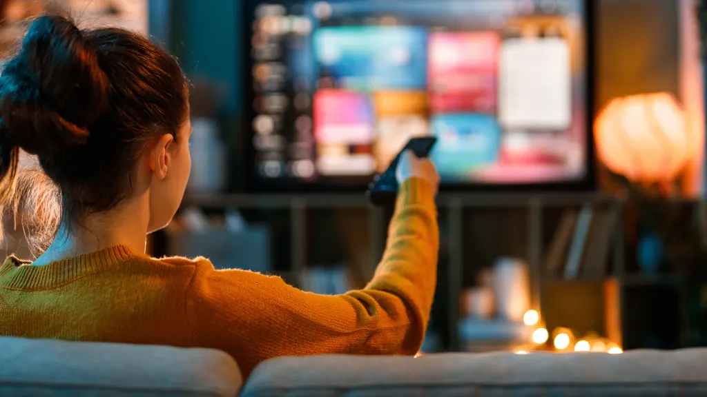 Over-the-shoulder photo of a woman pointing a remote at a TV screen