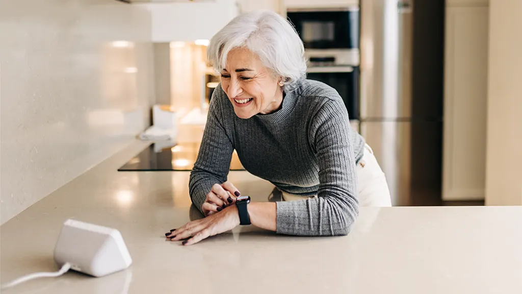 A mature woman using an Alexa-enabled smart speaker in her kitchen