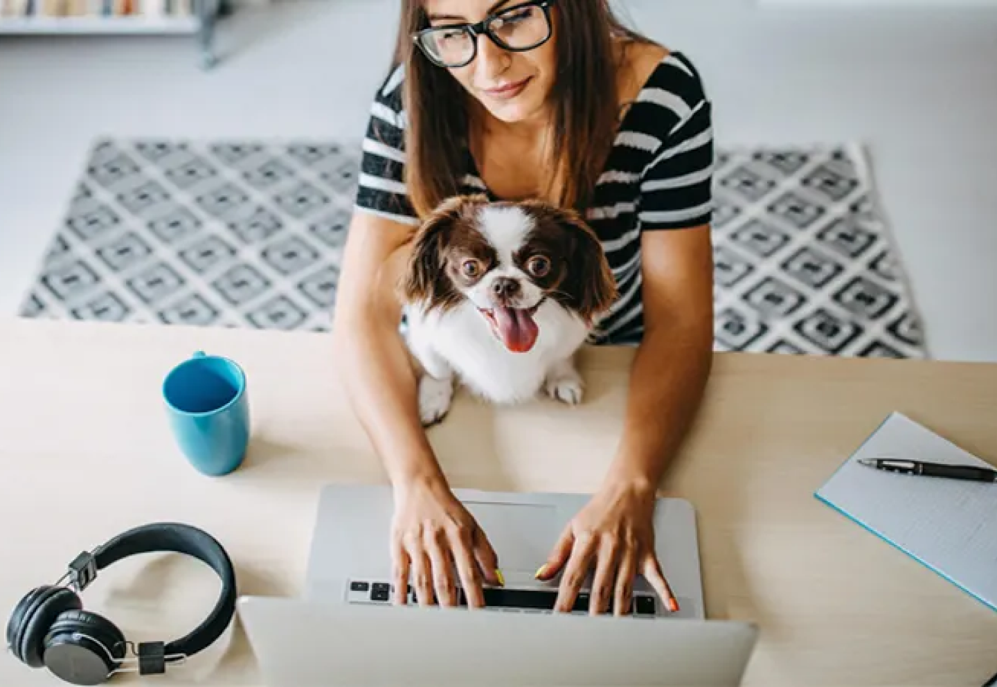 A woman working on a laptop with a dog on her lap