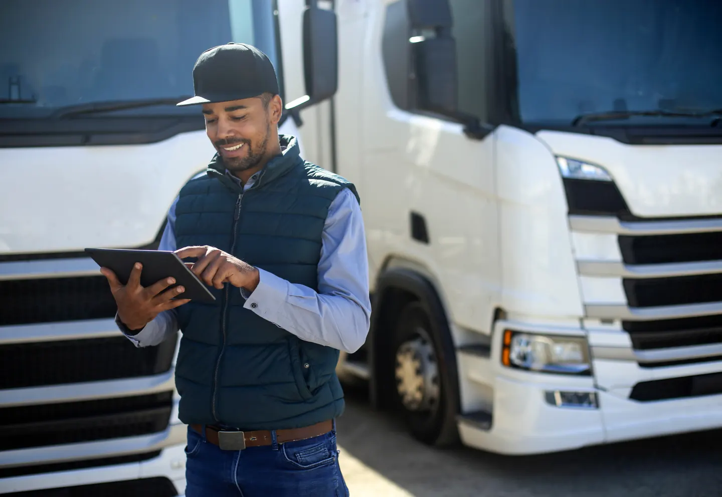 Delivery driver using a tablet while standing in front of semi-trucks.