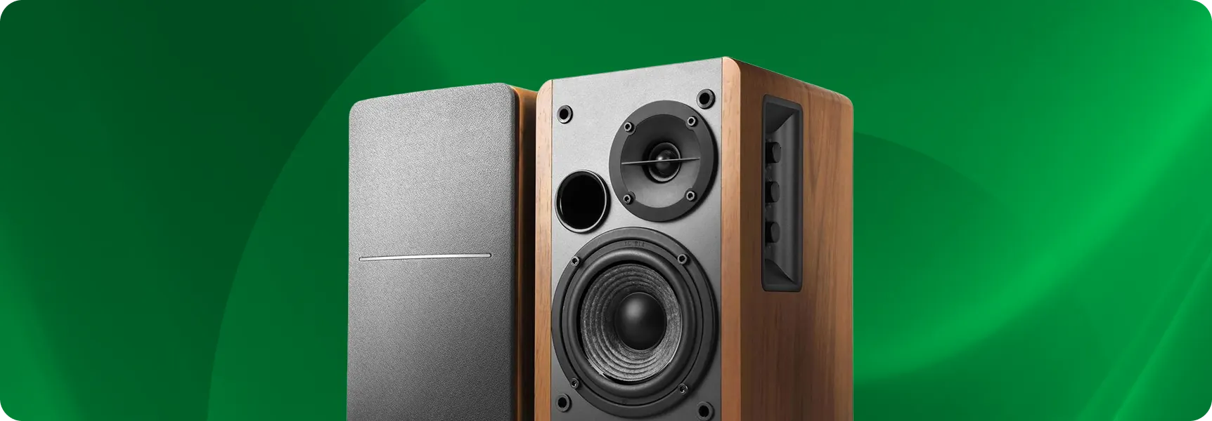 Pair of wooden bookshelf speakers with visible drivers on a green background.