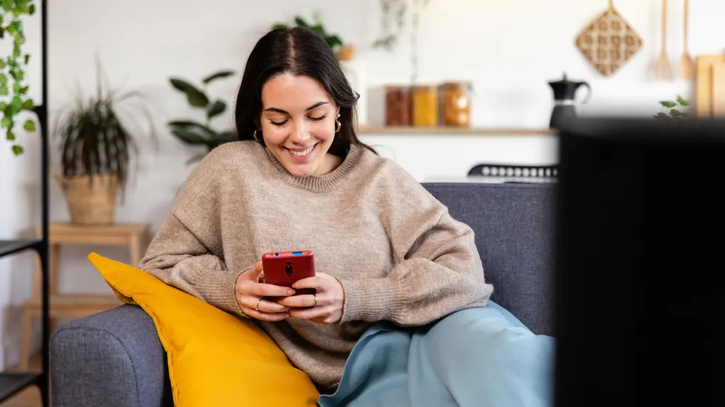 Smiling brunette woman looking down at a red smartphone in her hands