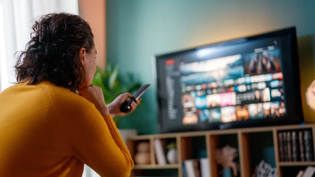 Woman in yellow sweater pointing a remote at a TV