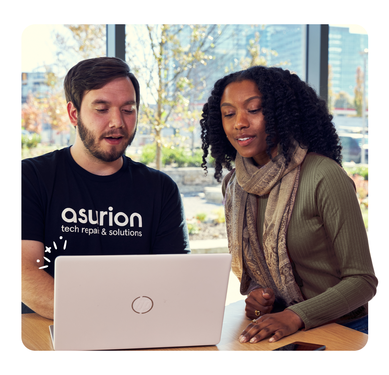 Asurion Tech Repairs & Solutions expert helping service member with laptop and phone in Exchange store on base