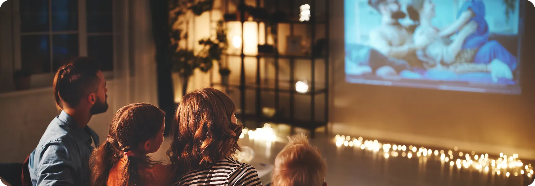 Family watching a movie projected on a wall in a cozy living room.