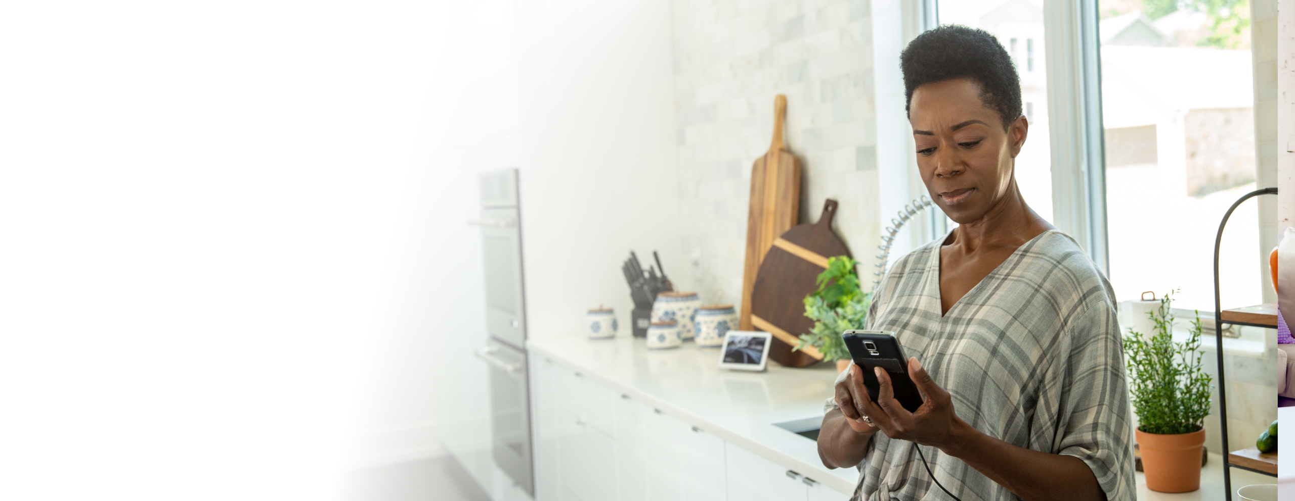 Woman standing in her kitchen looking at her phone while it's charging