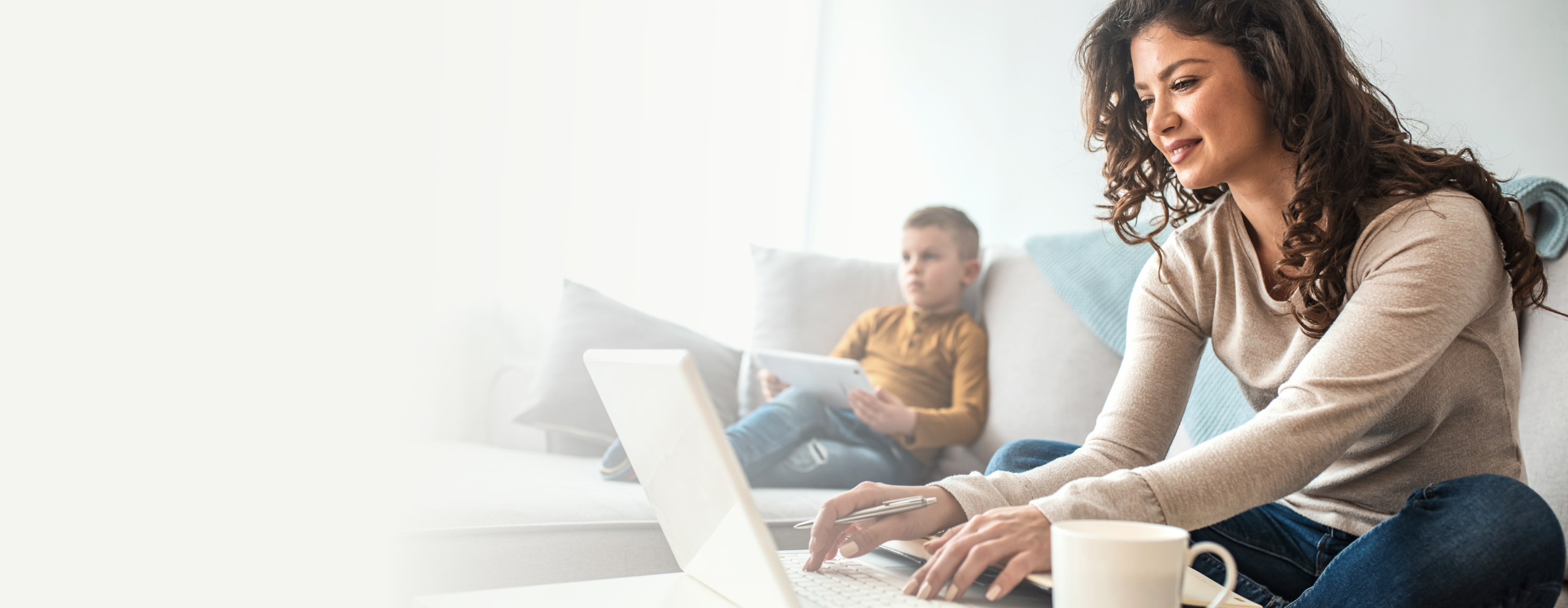 Woman on laptop and son using tablet in living room