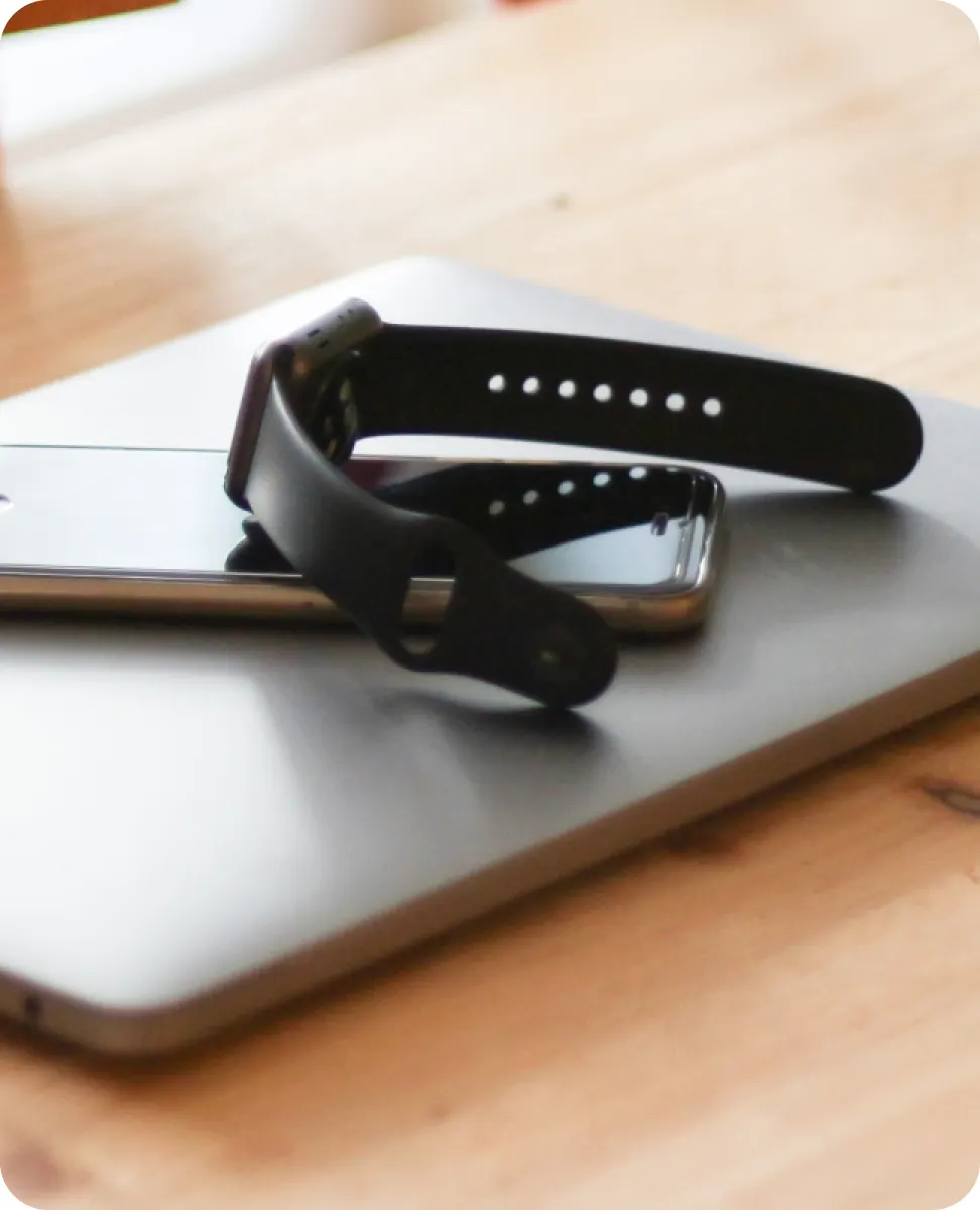 A smartwatch, phone, and laptop sitting on a table.