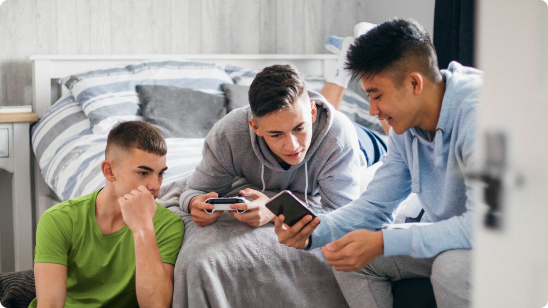 Three boys looking at a cellphone while sitting and laying on a bed